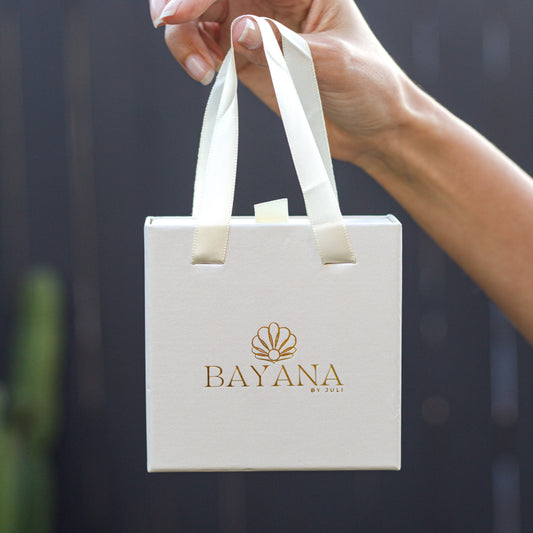 White gift bag with 'BAYANA' logo held by a hand against a dark background